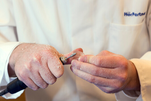 Ein Hörakustiker schleift eine Ohrpassform für ein individuell angepasstes Hörgerät.